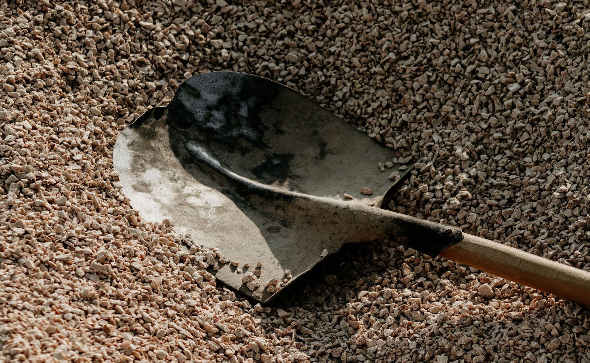 A metal shovel lying on a pile of small pebbles, suggesting outdoor landscaping or construction activities.